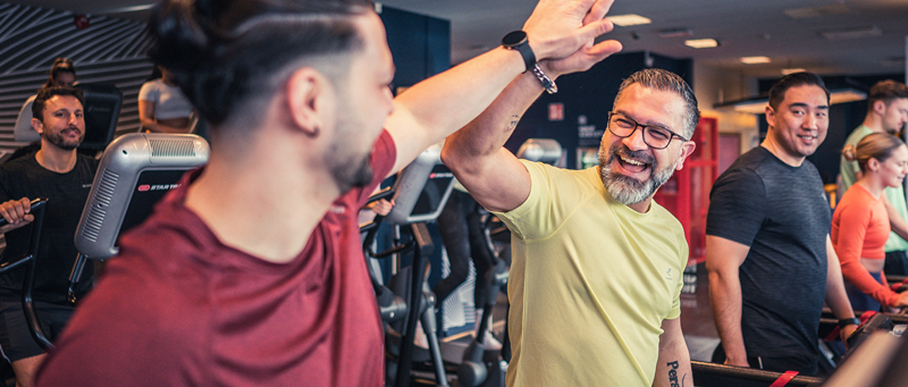 två män gör high five på löpbandet på gymmet
