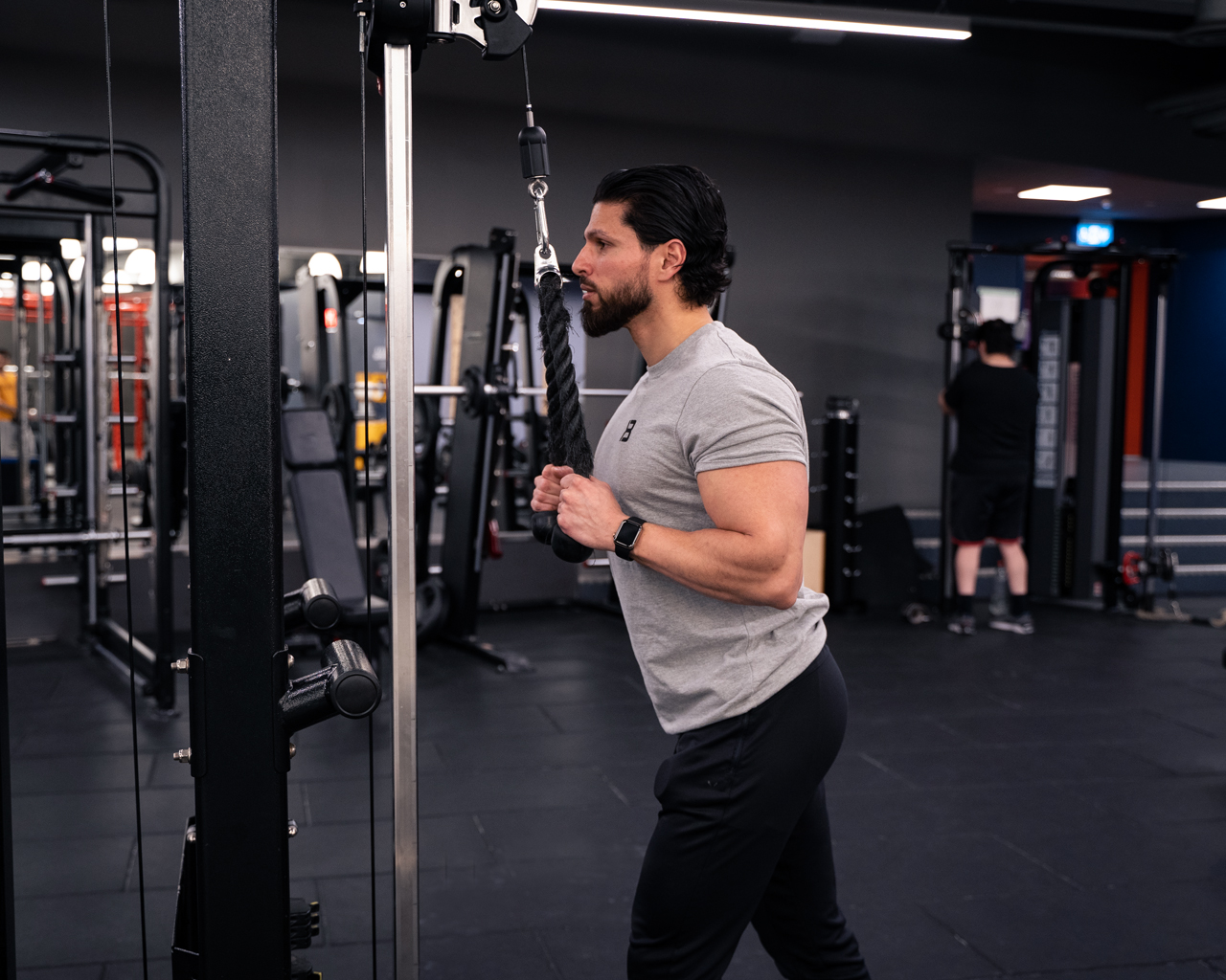 Man i startposition för triceps pushdowns med rep i cablemaskin – armbågarna böjda och nära kroppen