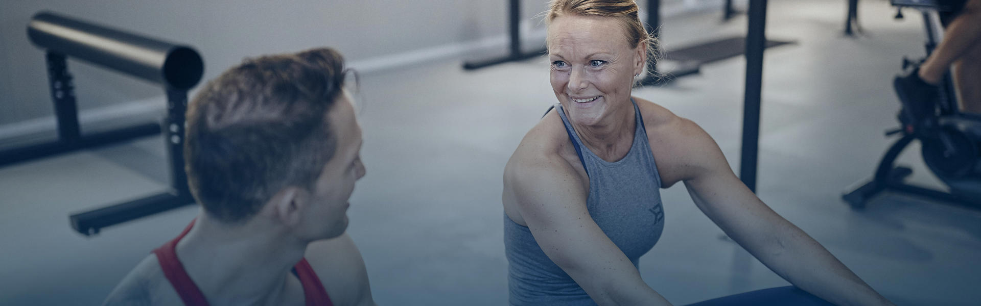 A man and a woman sitting in a gym smiling and talking while using the row machine.