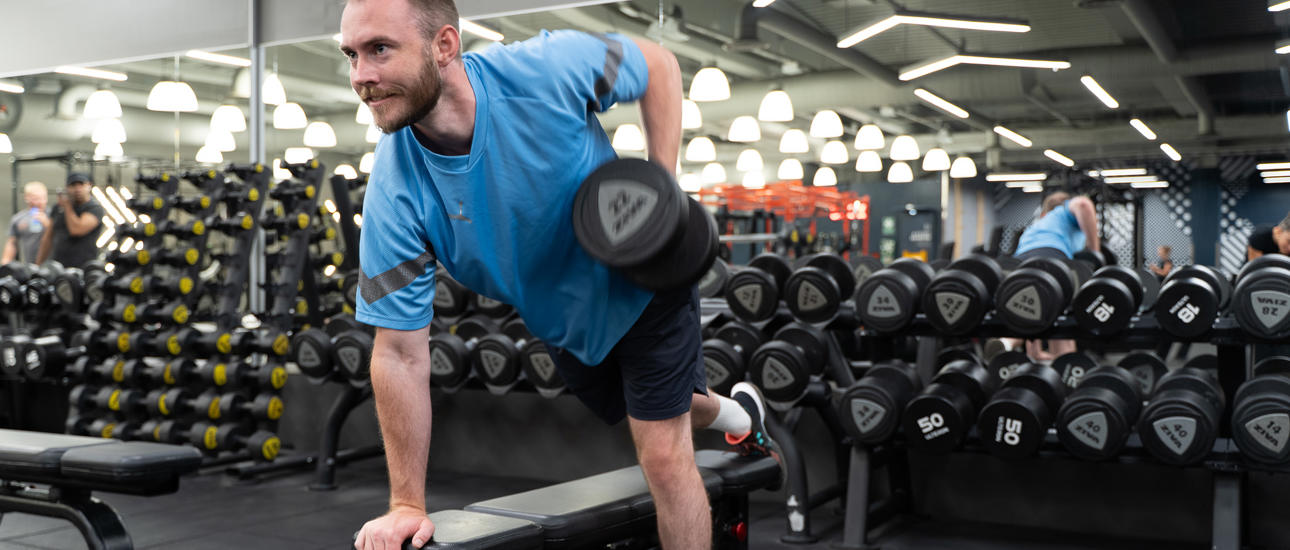 Man gjør hantelroing på benk på treningssenter