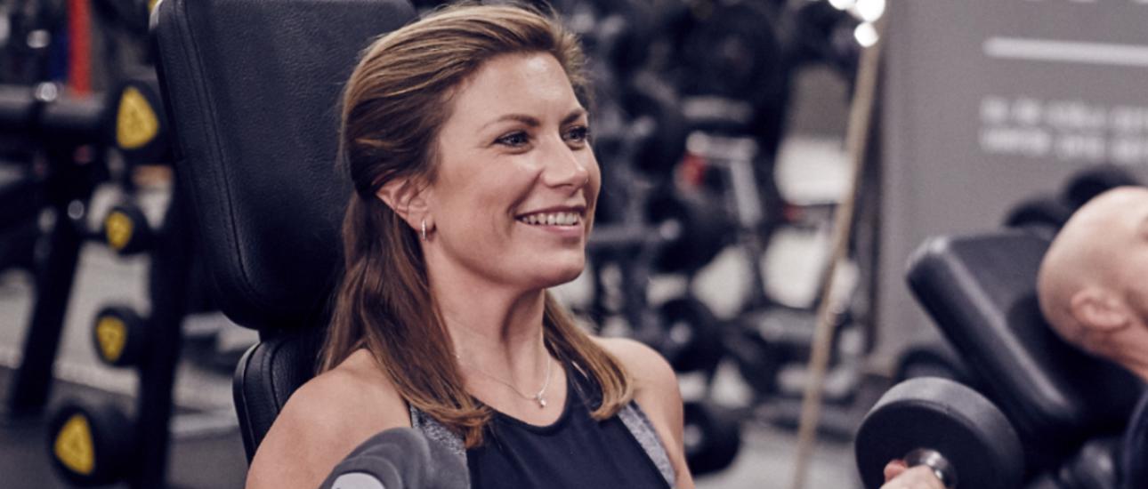 Sitting girl using dumbbells at the gym and smiling 
