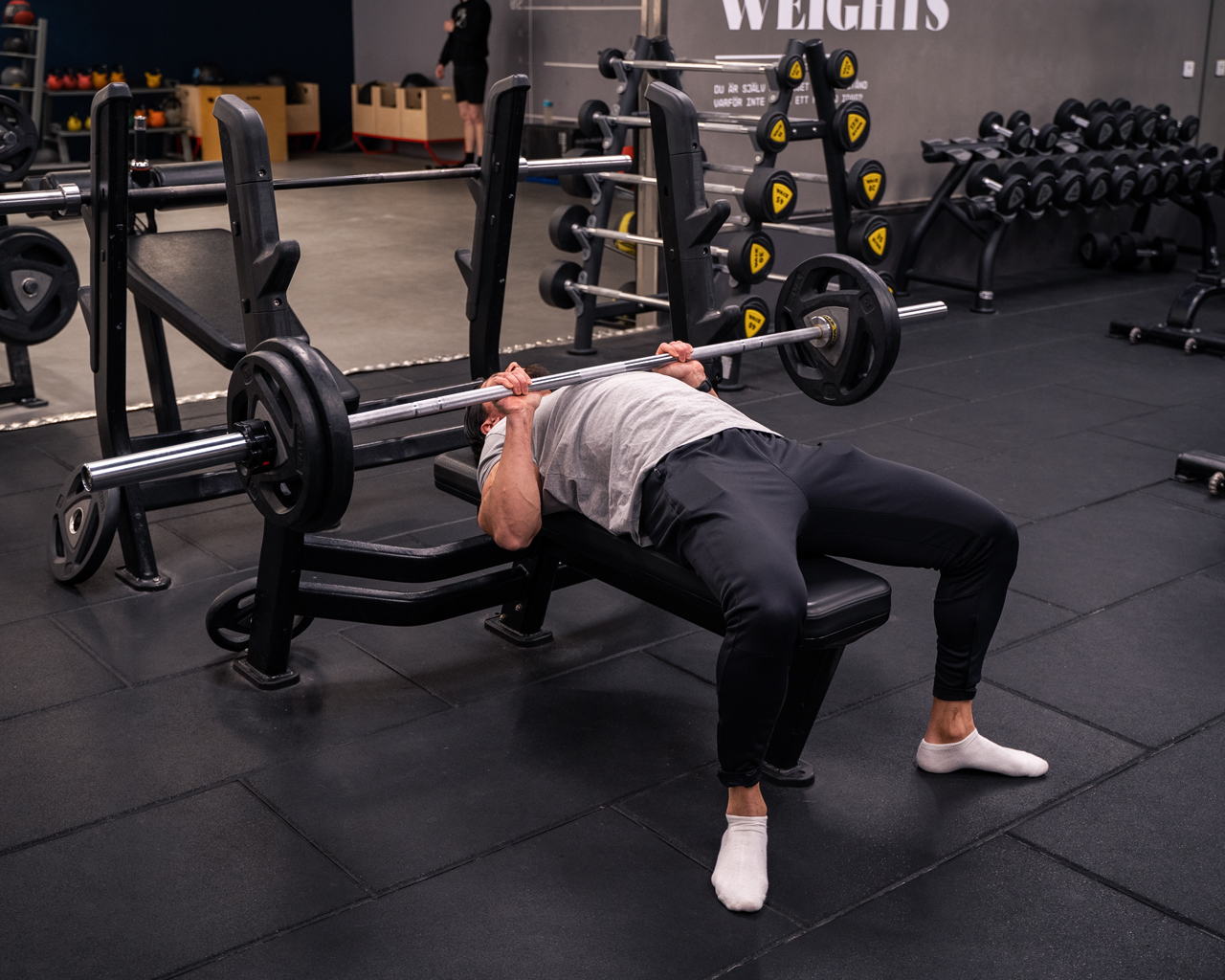 Man gör bänkpress med skivstång – pressövning för triceps