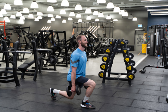 Man på Gym gör Utfallssteg med bakåtsteg